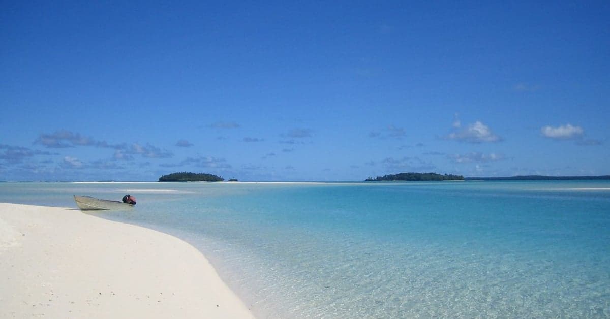 A wooden canoe on a white sand spit beside a turquoise lagoon