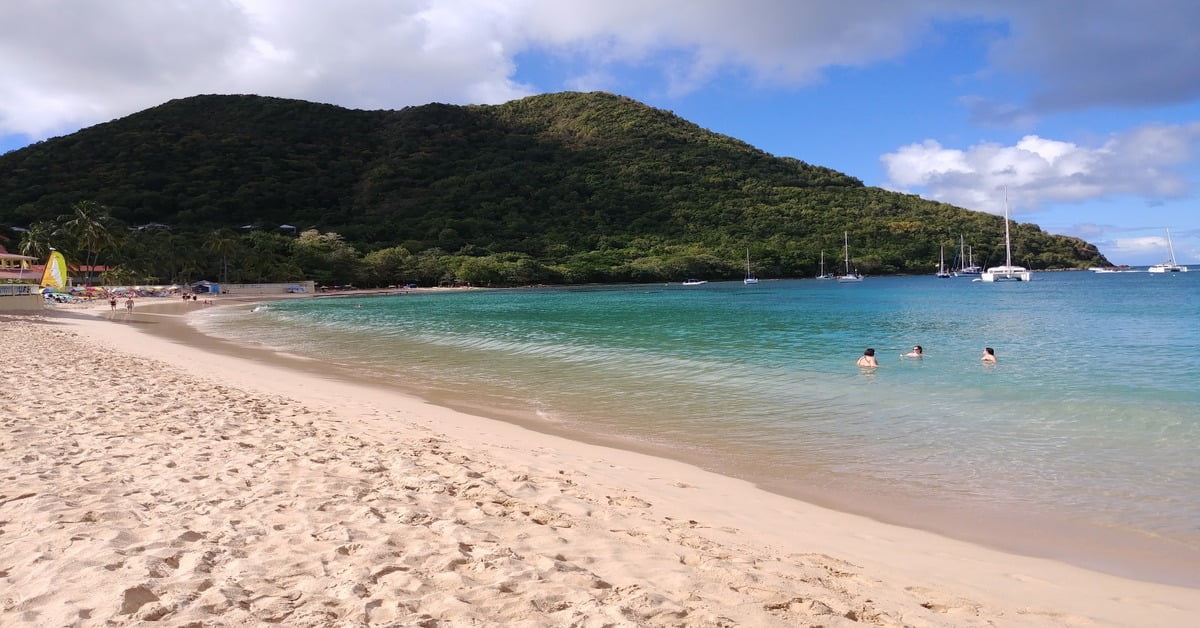 Reduit Beach in St. Lucia with golden sand, calm water, and lush green hills in the background